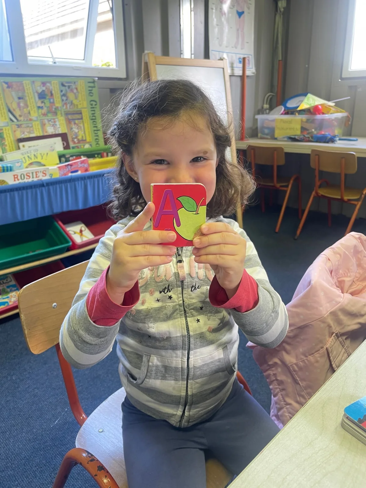 A young learner holding an apple alphabet card in the classroom